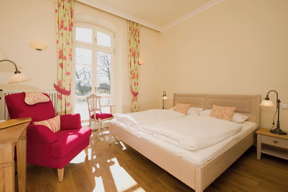 Ein Schlafzimmer mit einem großen Bett, einem Schreibtisch, einem Stuhl und einem Fenster mit Vorhängen.