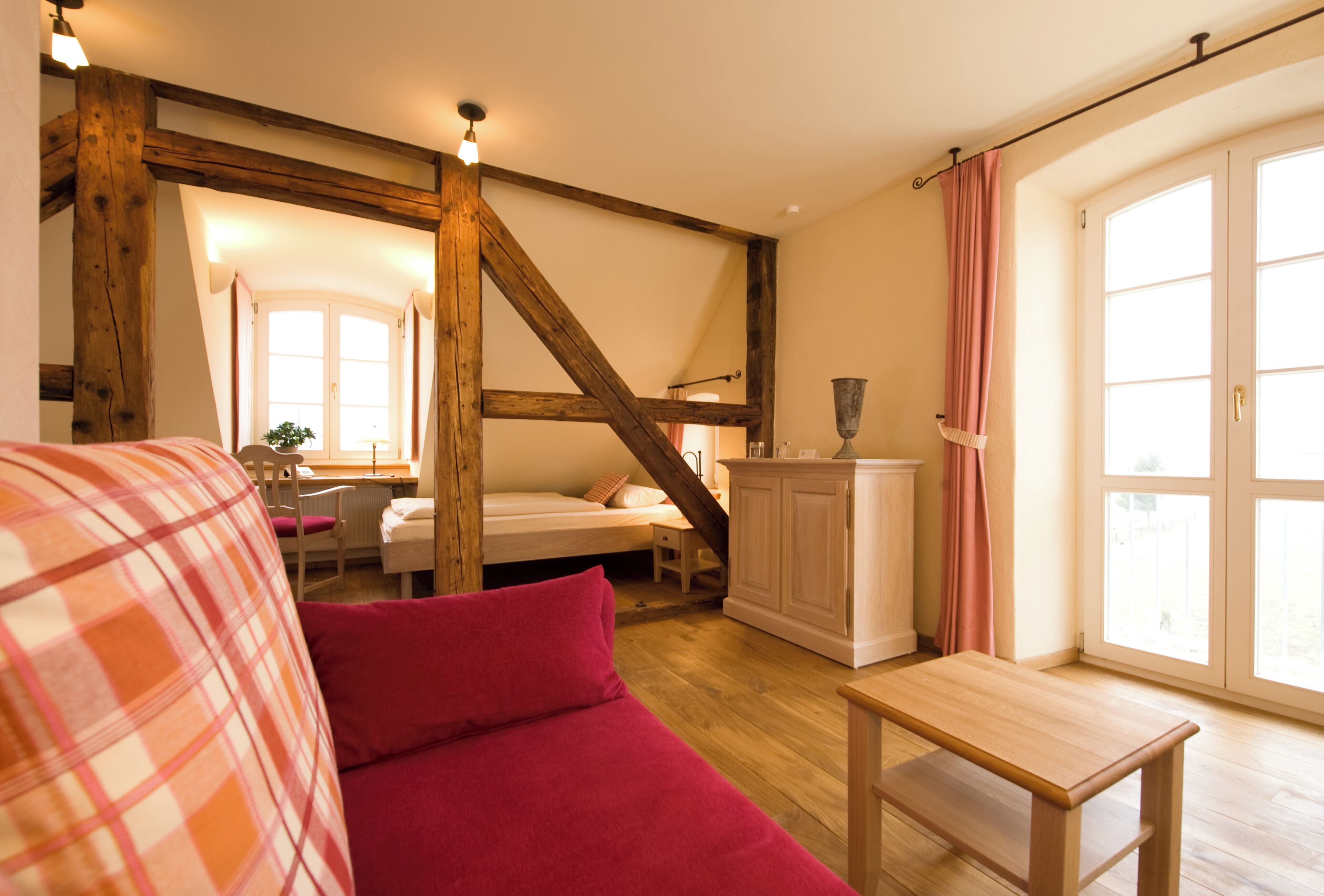 Une pièce confortable avec un lit, un banc en bois, une petite table et une fenêtre avec des rideaux.