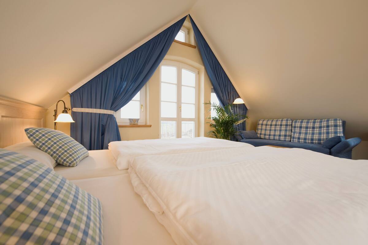 Ein Schlafzimmer mit einem großen Bett, einem kleineren Bett, einem Sofa und einem Fenster mit Vorhängen.