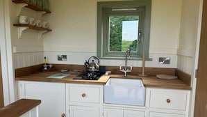 A compact kitchen with white cabinetry, a wooden countertop, a kettle, and a window above the sink. - Luxury Shepherds Hut set in a Countryside Setting (Southampton)