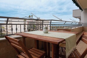 A balcony with a wooden table and chairs, a white vase, and a view of buildings and palm trees.