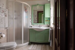 A bathroom with a shower, toilet, sink, and green cabinets.