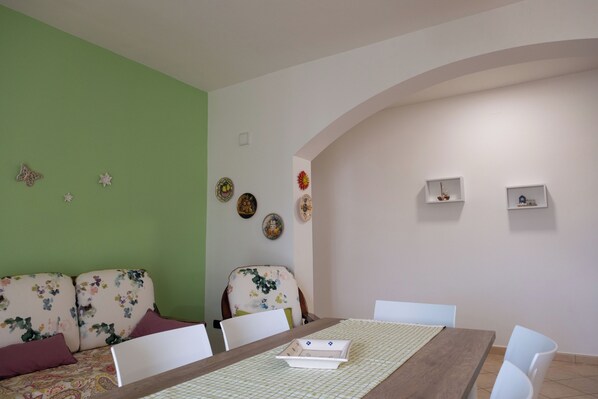 A dining area with a wooden table, white chairs, a floral sofa, and decorative plates on the walls.