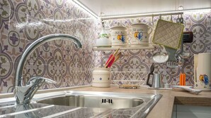 Una cocina con un lavamanos de acero inoxidable, un salpicadero decorativo y diversos utensilios y recipientes de cocina.