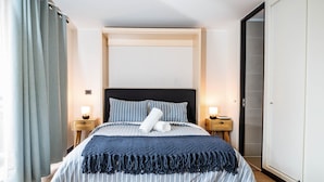 Un dormitorio ordenado con una cama, dos mesitas de noche, un armario y una puerta.