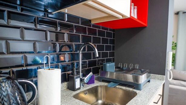 A modern kitchen with a stainless steel sink, black tiled backsplash, and a red cabinet. -  Almagro Spot by Andes+ (Santiago)