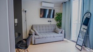 Una sala de estar moderna con un sofá gris, una silla negra, una mesita redonda pequeña, un espejo grande y una planta en maceta.