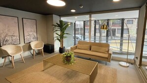 A modern living room with a beige sofa, two armchairs, a coffee table with a plant, and large windows offering a view of the street. -  Almagro Spot by Andes+ (Santiago)