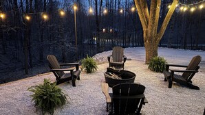 Ein Sitzbereich im Freien mit Adirondack-Stühlen, einer Feuerstelle und Lichterketten.