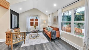 A spacious living room with a high ceiling, a wooden sofa, a wooden chair, a coffee table, and a large window with a view of the outdoors. - Modern Luxe 5 BR  4 BA home. Near the  Airport and Downtown Atlanta (Atlanta)