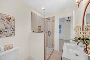 A modern bathroom with a glass-enclosed shower, a white sink with a mirror, and a decorative orchid arrangement.