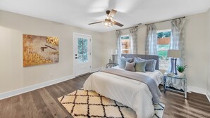 A bedroom with a bed, a ceiling fan, a window with curtains, a door, and a painting on the wall. - Modern Luxe 5 BR  4 BA home. Near the  Airport and Downtown Atlanta (Atlanta)