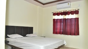 A single bed with a dark headboard, white bedding, and a window with red curtains. - Hotel Kalika Residency - Akkalkot (Akalkot)