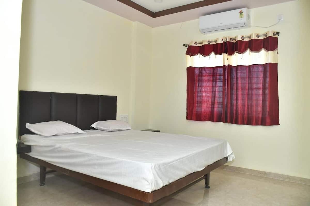 A single bed with a dark headboard, white bedding, and a window with red curtains.