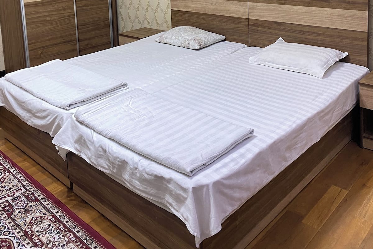 A neatly made bed with white linens, a wooden headboard, and a patterned wallpaper in the background.