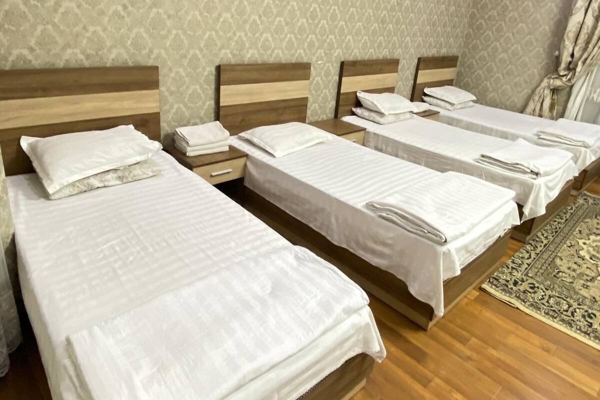 A hotel room with four beds arranged in a row, wooden headboards, and a patterned wallpaper.