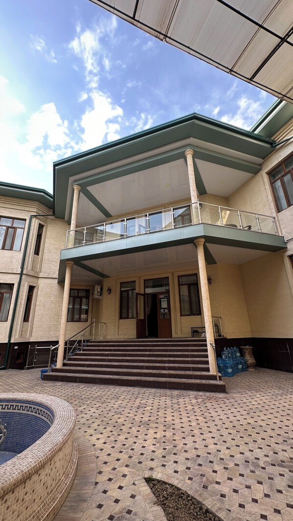 Un edificio con vestíbulo techado, piscina y patio con baldosas.