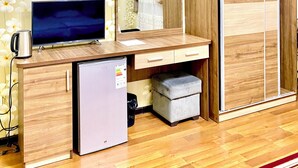 Een compacte kamer met een houten bureau, een televisie, een kleine koelkast en een kledingkast.