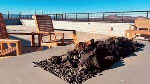 Une terrasse sur le toit, avec des chaises en bois, un foyer au charbon de bois et une vue sur les montagnes lointaines.