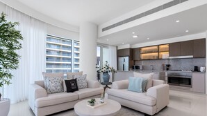 A modern living room with a beige sofa, a round coffee table, and a large window with curtains. - Waterfront Living w Unparalleled Sea Palm Vws (Dubai)