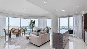 A modern living room with a dining area, a sofa, a coffee table, and a kitchen island. - Waterfront Living w Unparalleled Sea Palm Vws (Dubai)