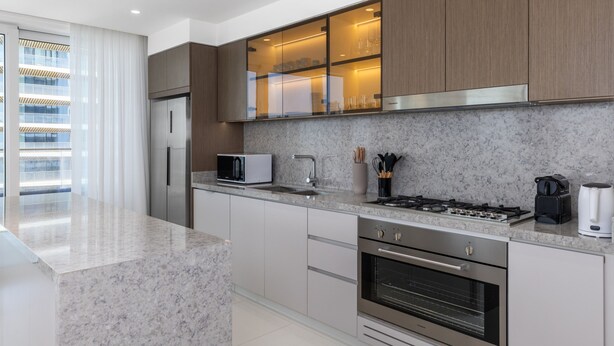 A modern kitchen with a granite countertop, stainless steel appliances, and wooden cabinets. - Waterfront Living w Unparalleled Sea Palm Vws (Dubai)
