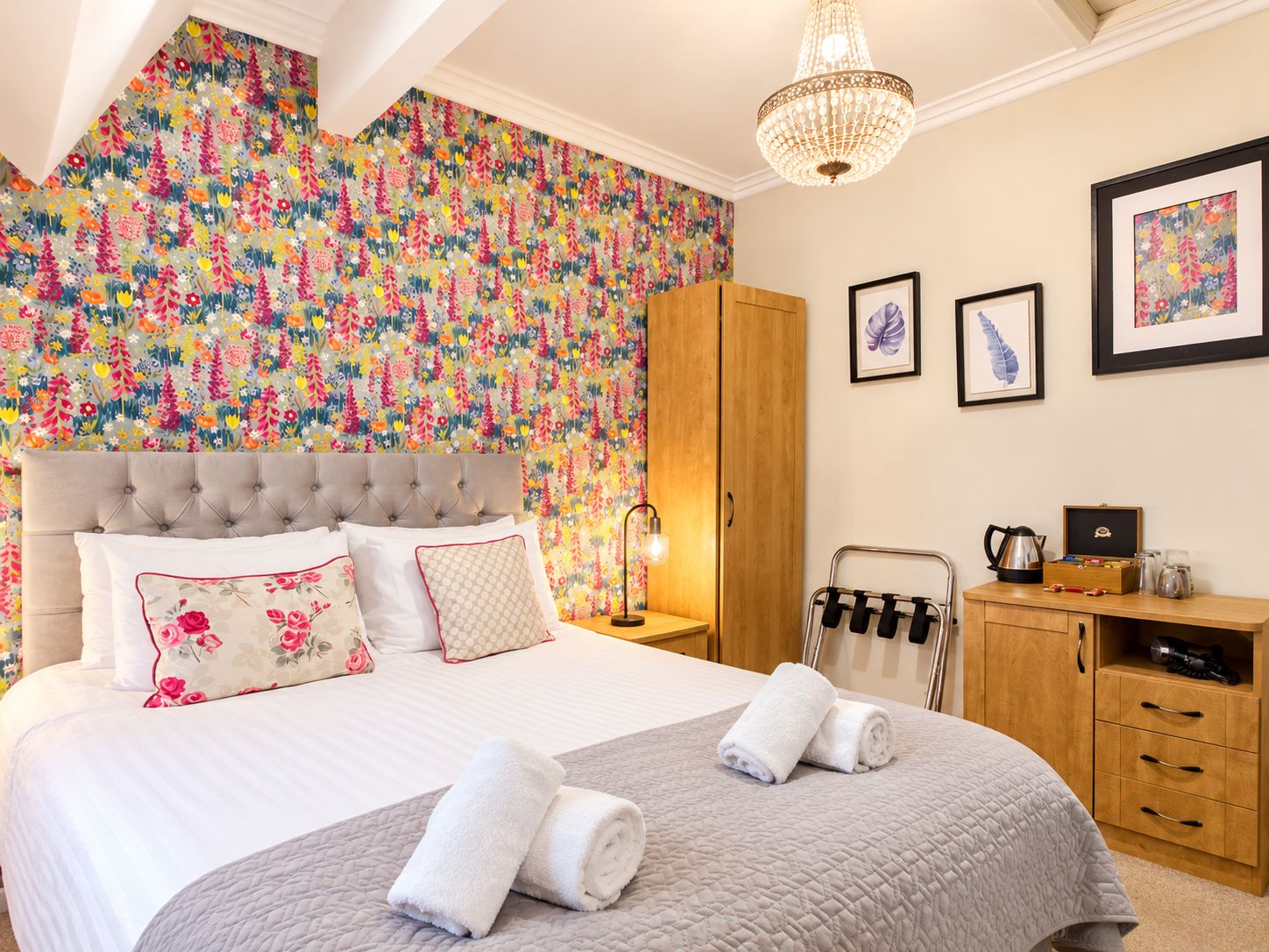 A hotel room with a large bed, a wardrobe, a bedside table with a lamp, and a chandelier.
