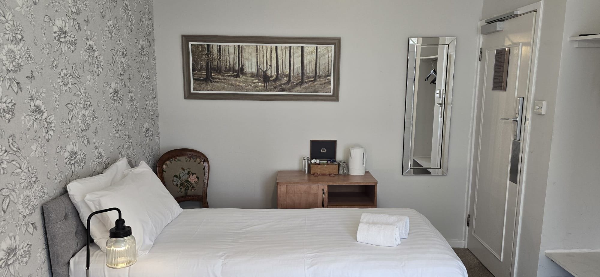 A hotel room with a bed, a nightstand, a framed picture, a wardrobe, and a mirror.