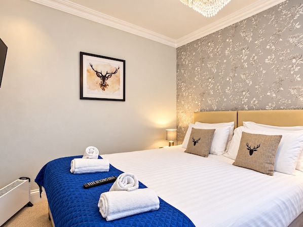 A hotel room with a large bed, a framed deer head artwork, and a floral wallpaper design. - The Coach House (Newcastle-upon-Tyne)