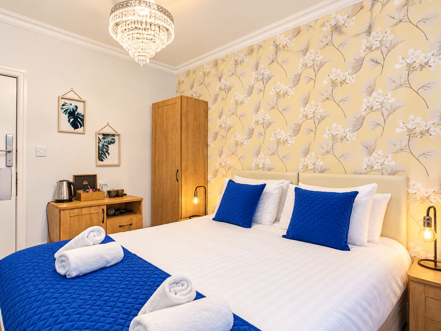 Habitación de hotel con una cama grande, un armario de madera, un escritorio con lámpara y un candelabro.