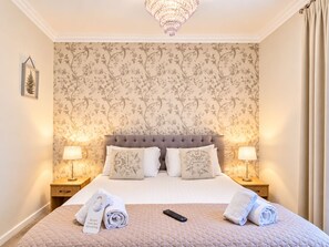 A hotel room with a large bed, two bedside lamps, a chandelier, floral wallpaper, and a sign indicating the room is free for servicing. - The Coach House (Newcastle-upon-Tyne)