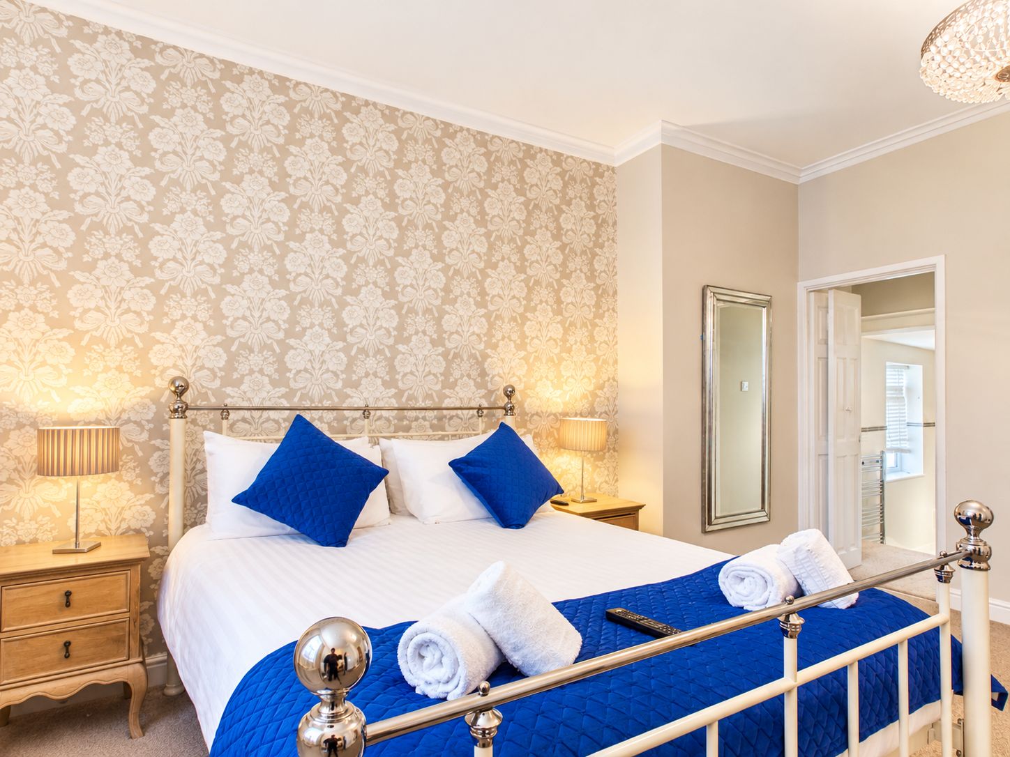 Una habitación de hotel con cama, mesitas de noche, un espejo y una puerta que da a otra habitación.