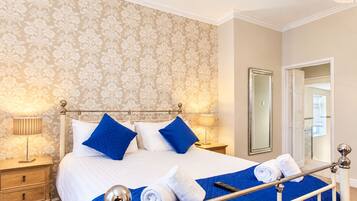 Una habitación de hotel con cama, mesitas de noche, un espejo y una puerta que da a otra habitación.