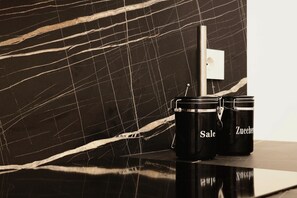 Two black containers with lids on a reflective surface, one labeled "Sale" and the other "Zucker," against a dark marble wall with white veining. - JOIVY Cute 1BR flat near the City Centre (Milan)