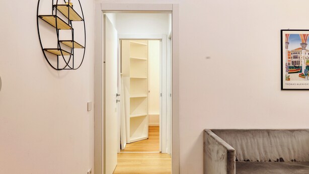 A hallway with a wooden floor, a grey sofa, and a wall-mounted shelf unit.