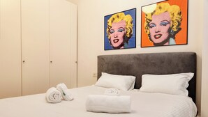 A hotel room with a bed, two white towels, a rolled-up towel, and two paintings on the wall.