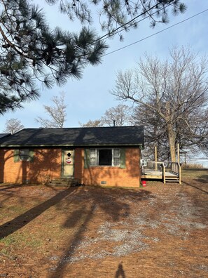 A small brick house with a wooden deck, a garage door, and a mailbox.