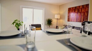 Een eethoek met een tafel voor vier personen, een potplant en een lamp.