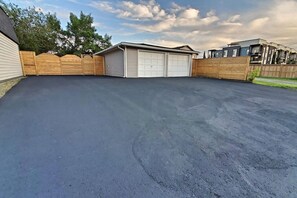 A residential garage with a dark-colored driveway, wooden fences, and a clear sky.