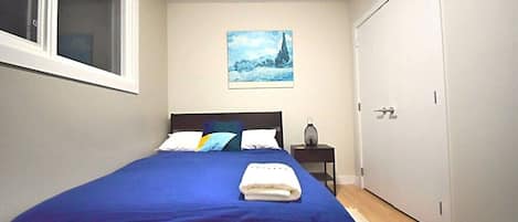 A bedroom with a single bed, a nightstand, a painting, and a door.