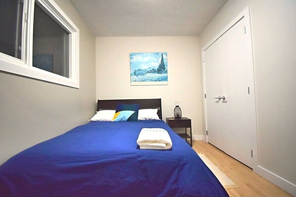 A bedroom with a single bed, a nightstand, a painting, and a door.