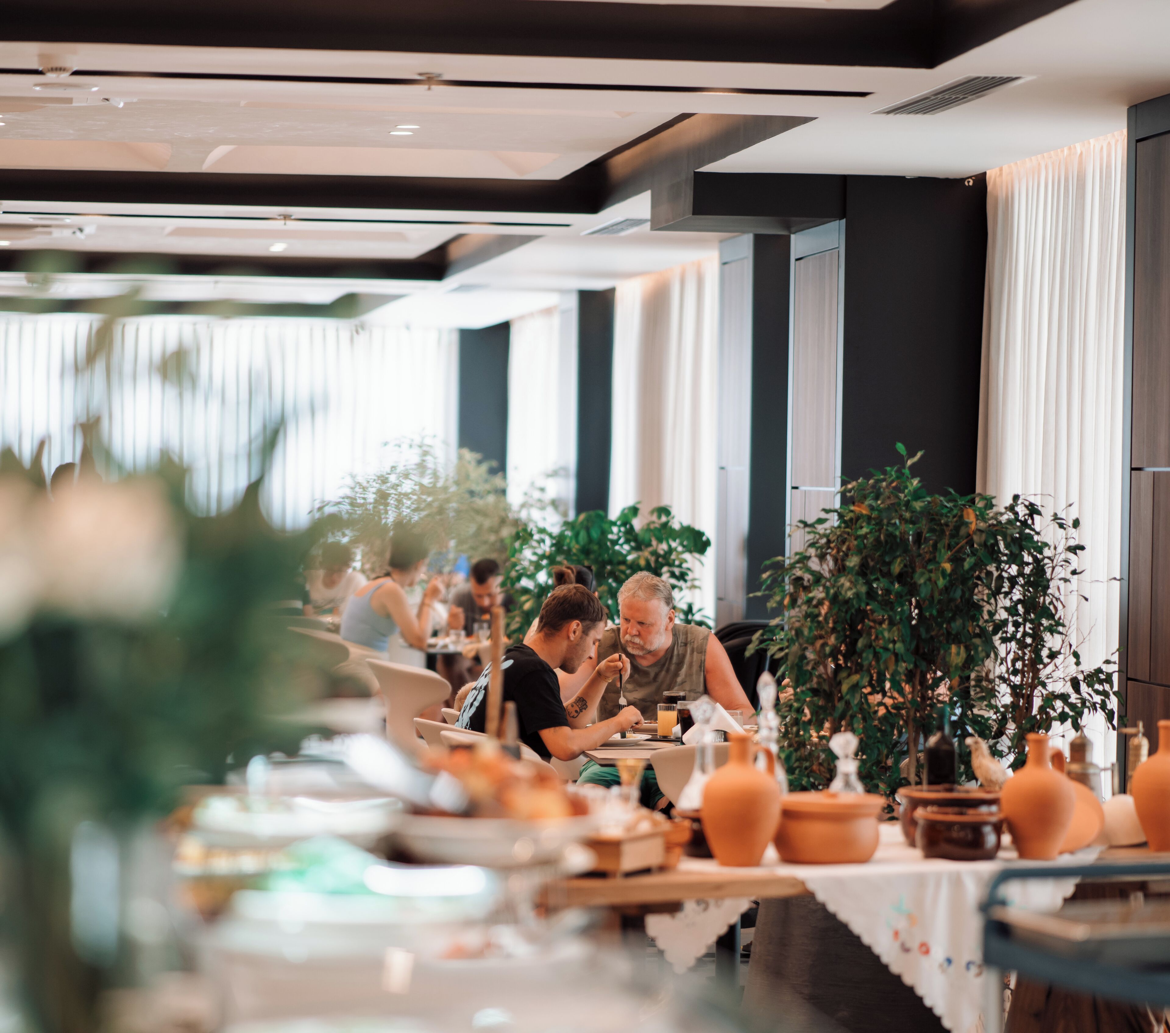 A dining area with tables set for a meal, featuring terracotta pots and a large potted plant.