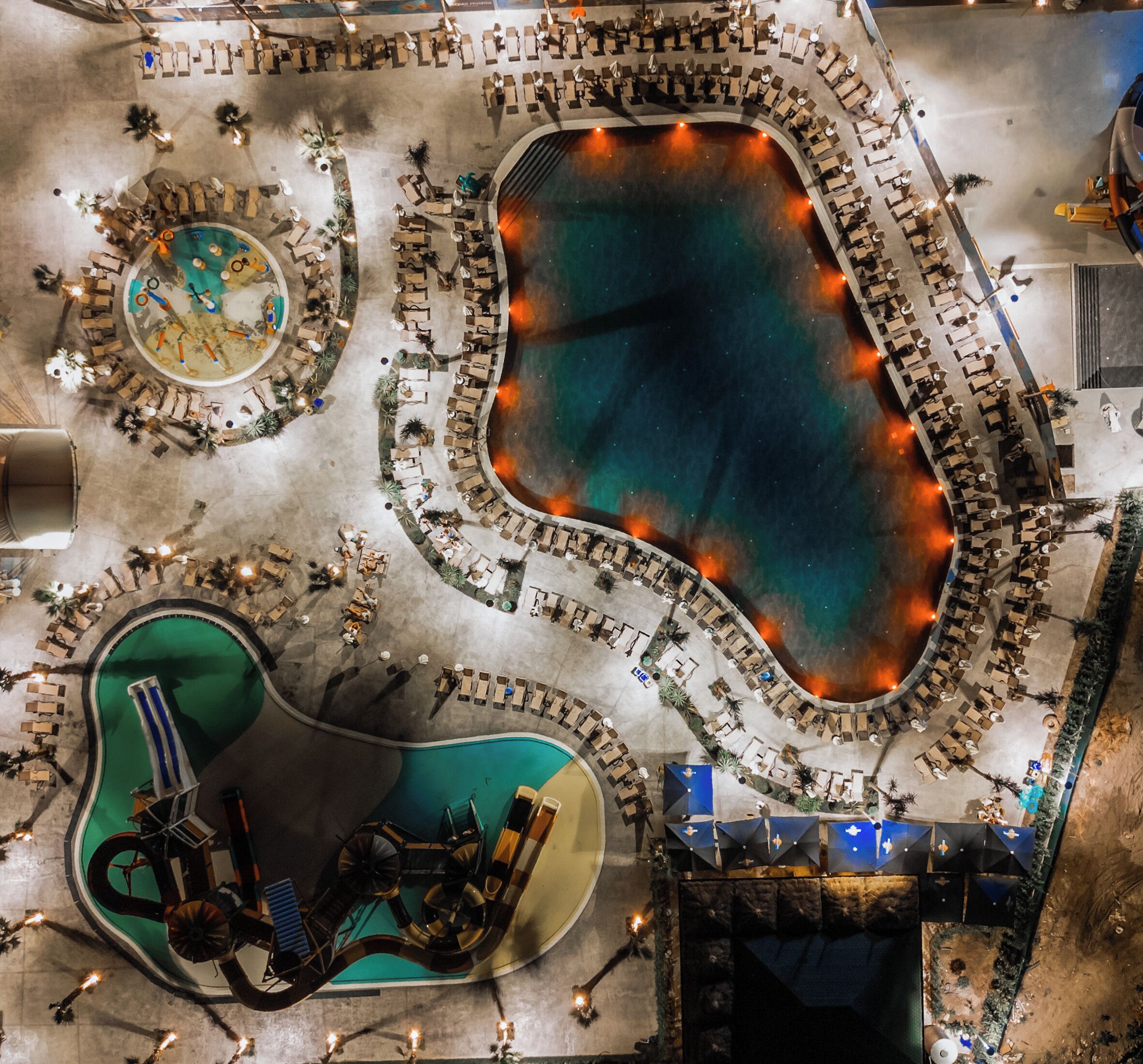An aerial view of a resort with multiple swimming pools, lounge areas, and a stage for events.