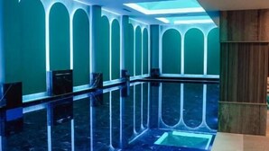 Um interior moderno com piso refletivo, paredes verde-água e iluminação de teto geométrica.
