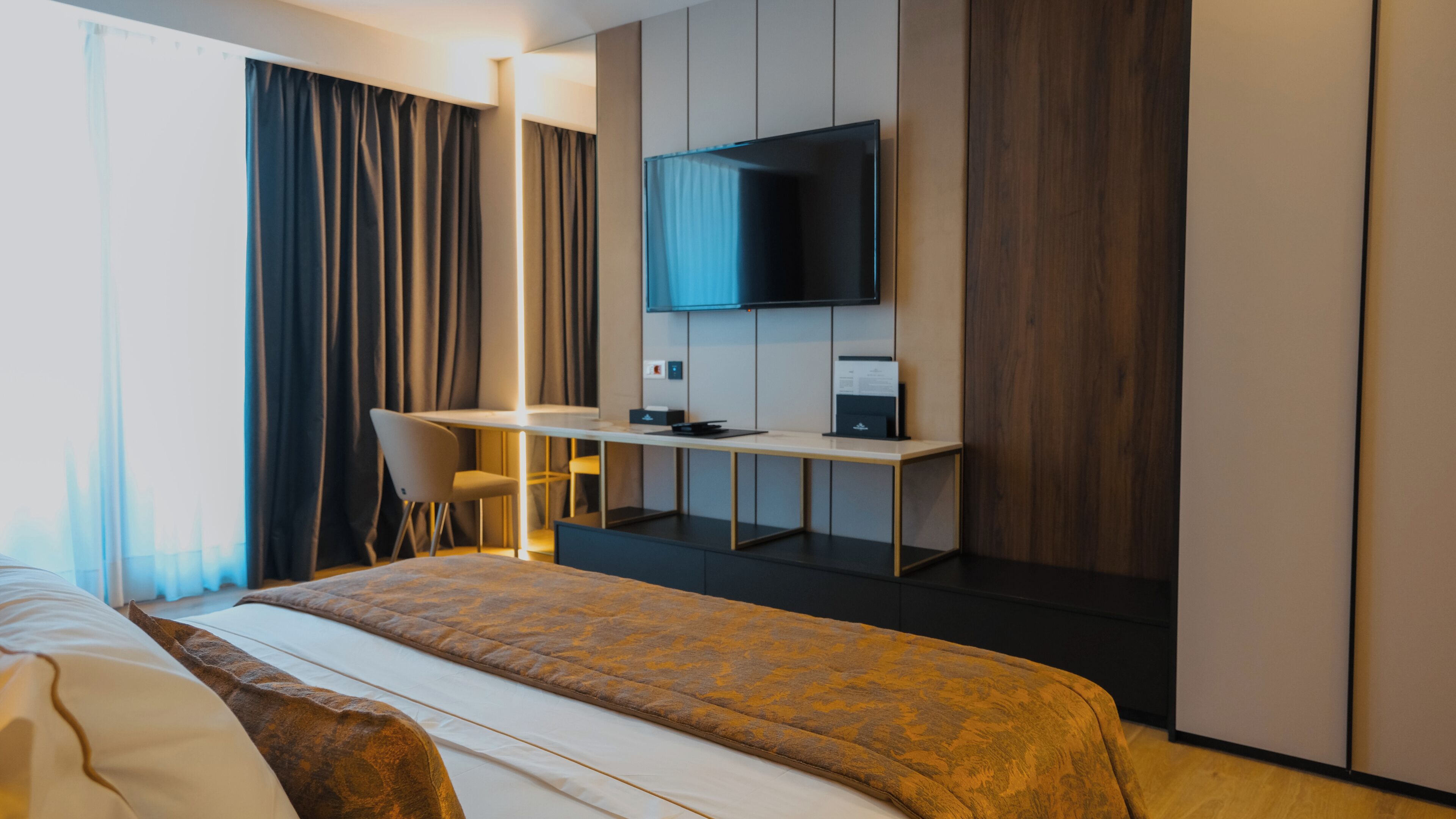 A hotel room with a bed, a desk, a chair, a television, and a wardrobe.