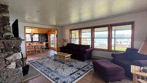 A spacious living room with a stone fireplace, a large window with a view of the water, and a cozy seating area with a rug.