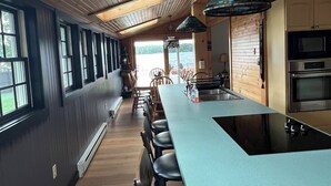 A modern kitchen with a long island, wooden ceiling, and large windows.