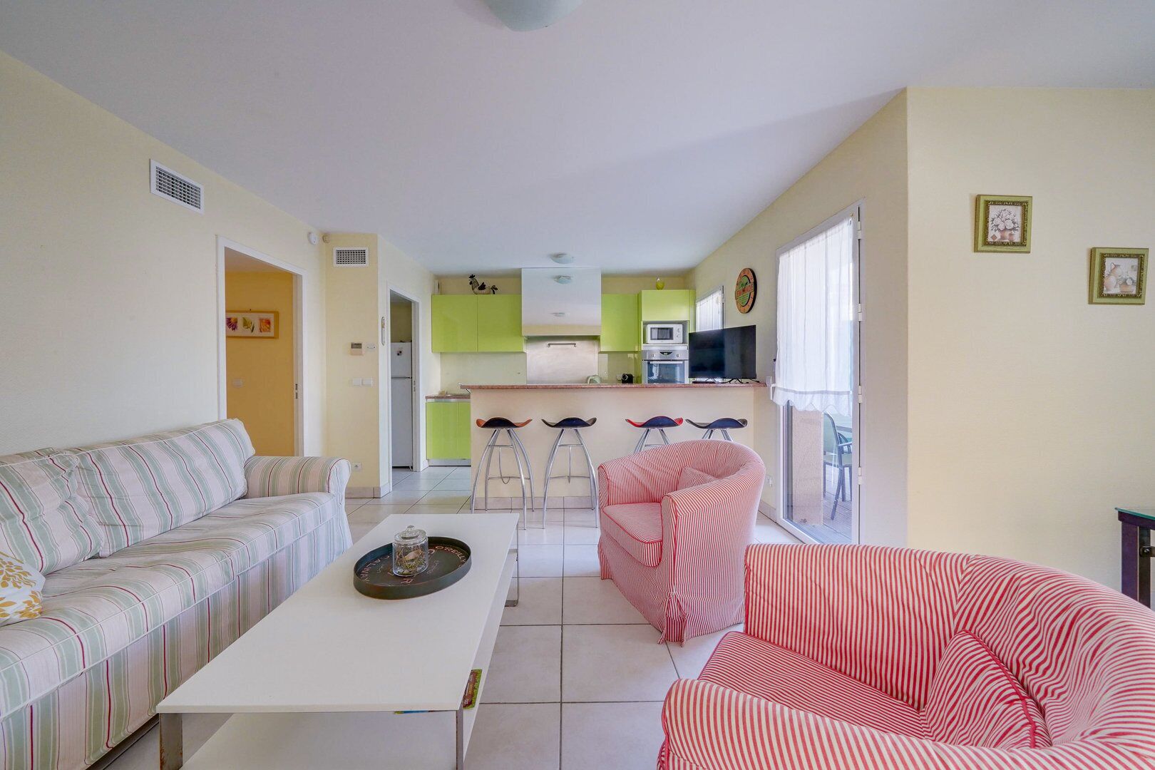 A living room with a sofa, a striped armchair, a coffee table, and a kitchen in the background.
