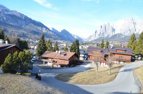 A mountain village with wooden houses, a winding road, and a view of snow-capped peaks.