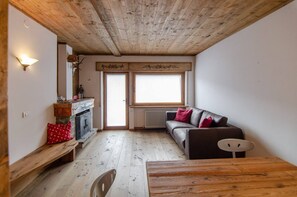 A cozy room with a wooden ceiling, a fireplace, a sofa, and a dining table. - Summer in the mountains (San Vito di Cadore)